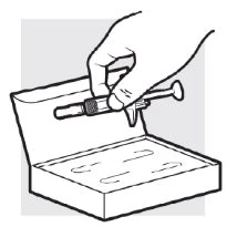 A hand holding a syringe-like medical device above an open box containing two horizontal vials