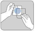 Two hands handling two transparent slides, overlapping them to prepare a sample on a gray background surface