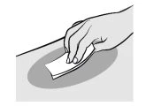 A hand holds a small folded white sheet of paper over a gray circular surface against a light background