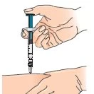 One hand holds a syringe with the needle pointing downward to inject medication into a person's arm resting on a surface