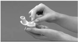 Due mani tengono e aprono un piccolo dispositivo medico bianco con un coperchio a scatto per prepararlo