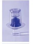 A transparent glass vial with cap and a liquid content of intense blue color against a light purple background