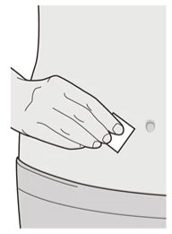 Una mano tiene un piccolo cerchio bianco e lo avvicina all'addome di una persona per applicarlo sulla pelle sopra l'ombelico