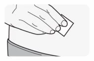 A hand holds a small rectangular adhesive patch and places it on the skin of the abdominal or back area