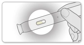 A hand holding a slender medical device with a small central viewing window showing a yellowish liquid inside