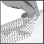 A hand lifts and folds a flap of a thin, evenly woven square medical mesh on a light-colored surface