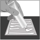 A hand squeezes a cream tube to apply a white product strip onto a square-grid surface