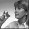 A woman attentively looks at an asthma inhaler held up with her left hand in front of her face in a black-and-white photo