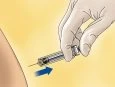 A gloved hand holding a syringe inserted into the body with a downward-pointing blue arrow indicating the direction of movement