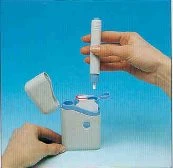 A hand holding a white injectable pen above an open matching container on a uniform light blue background