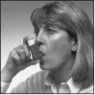A woman with light-colored hair holds a box of medication close to her mouth, ready to take a tablet
