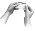 Two hands holding and opening a medication blister pack to remove a single tablet or capsule from the metallic packaging