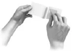 Two hands holding and unfolding a small folded paper leaflet or a white paper container against a neutral background