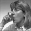 Woman with light hair holding a small box close to her open mouth as if taking a medication or supplement