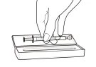 Black line drawing of a hand holding a syringe horizontally above an open rectangular box with an inner container