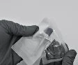 Ręka w rękawiczce trzyma przezroczyste opakowanie plastikowe zawierające fiolkę z lekiem na neutralnym szarym tle