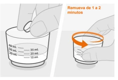 Una mano inserisce una compressa in un bicchiere graduato con acqua e un