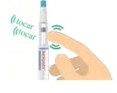 Una mano tocca un dispositivo medico cilindrico bianco e azzurro con linee verdi che indicano il punto di pressione per l'attivazione