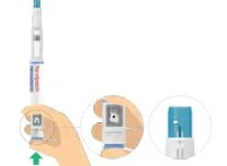 A hand holds a medical injector pen with a green arrow pointing toward the