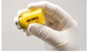 A white-gloved hand firmly holds a vial with clear yellow liquid against a light neutral background