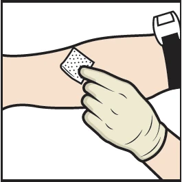 Una mano guantata applica un cerotto quadrato traforato sulla pelle di un braccio disteso con un dispositivo medico visibile in alto a destra