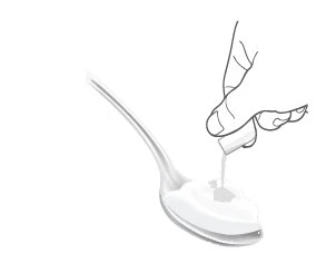 Una mano sostiene una pastilla blanca sobre una cuchara que contiene líquido para la administración oral
