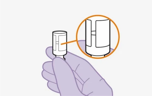 A gloved hand holding a white medical device with a circular magnification showing a detailed view of the upper part of the device