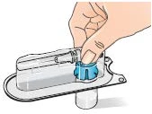 Una mano tiene e preme il cappuccio blu di un dispositivo medico trasparente montato su una base piatta con un piccolo cilindro inferiore