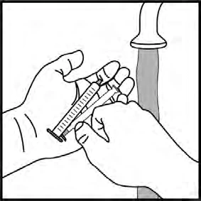 Due mani tengono una siringa con ago e liquido per preparare l'iniezione accanto a un flacone di medicinale aperto