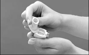 Two hands hold and open a cylindrical white medical device with an upper cap for the
