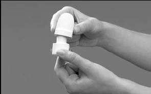 Two hands separate a white medical device composed of an upper cap and a cylindrical base on a neutral gray background