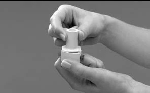 Two hands hold and manipulate a cylindrical white medical device composed of two interlocking parts on a gray background