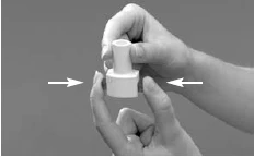 One hand holds a white medical device while two white arrows indicate lateral pressure to be applied with the fingers