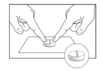Dos manos con los índices extendidos presionan sobre una pastilla circular dividida por la mitad colocada sobre una superficie plana, con detalle ampliado de la pastilla