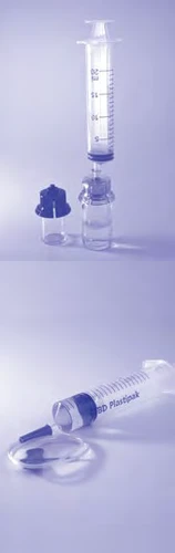 Transparent syringe with graduations placed above a glass vial with blue cap and a second syringe lying on a light surface