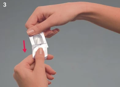 Two hands carefully opening a small white aluminum pouch following the direction indicated by a vertical red arrow