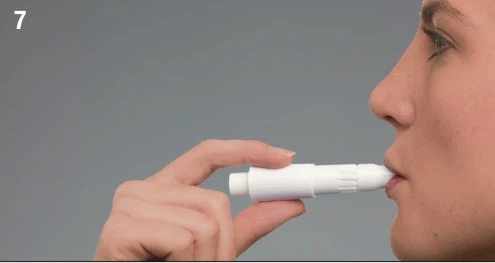 Profile view of a person holding a white medical device between the lips for inhalation