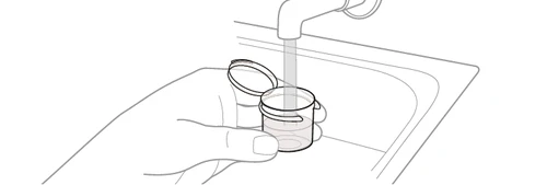 Una mano tiene un contenitore sotto un rubinetto aperto con acqua che scorre all'interno di un lavandino bianco