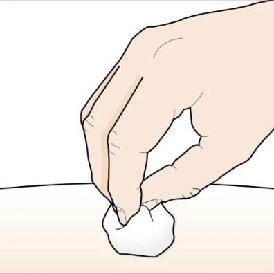 A hand holding a white cotton ball and gently pressing it against a light skin surface