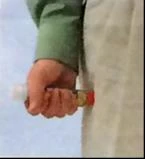 A hand firmly holds a small glass vial with a red cap against the side of a person wearing a green shirt and an apron