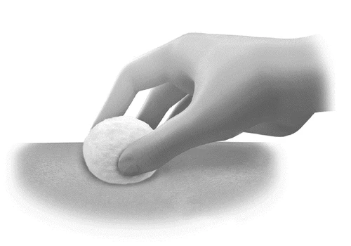 A hand holds a white cotton pad and gently presses it against a light, smooth skin surface