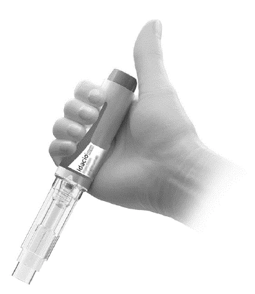 A hand vertically holding a cylindrical medical device with the Idacio brand and a transparent base