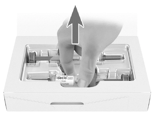 A hand lifts a prefilled syringe Idacio from a white plastic tray