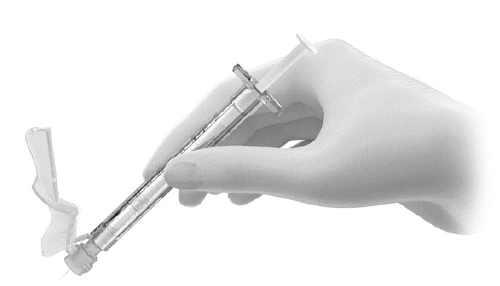 A hand holding a syringe with needle and open protective cap ready for drug administration in a medical procedure