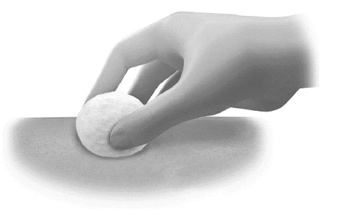 A hand holding a small round white tablet above a flat light surface in a