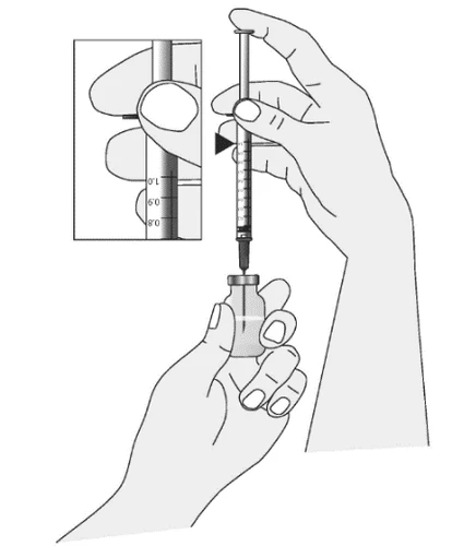 A hand holding a syringe with needle above a glass vial while the