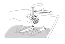 Una mano lava un cappuccio di una siringa sotto il getto d'acqua di un rubinetto sopra un lavandino con altre siringhe all'interno