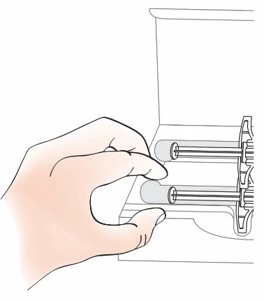 A hand holding two horizontal syringes with gray plungers placed on a white surface next to a tall container