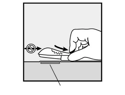 Disegno tecnico che mostra una mano che preme la parte superiore di un dispositivo medico piatto con piccoli fori su una superficie orizzontale