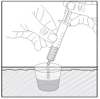Two hands hold a syringe with a needle to aspirate liquid contained in a small transparent container on a flat surface